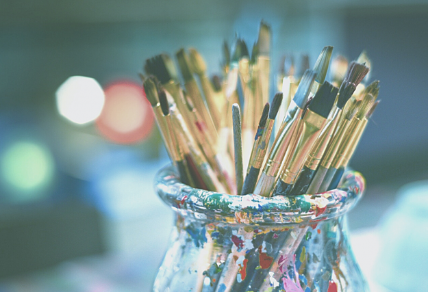 paintbrushes in a glass jar against a blue background